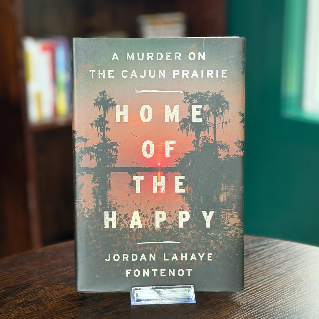 Book titled 'Home of the Happy' by Jordan Lahaye Fontenot on a wooden surface with a blurred background.