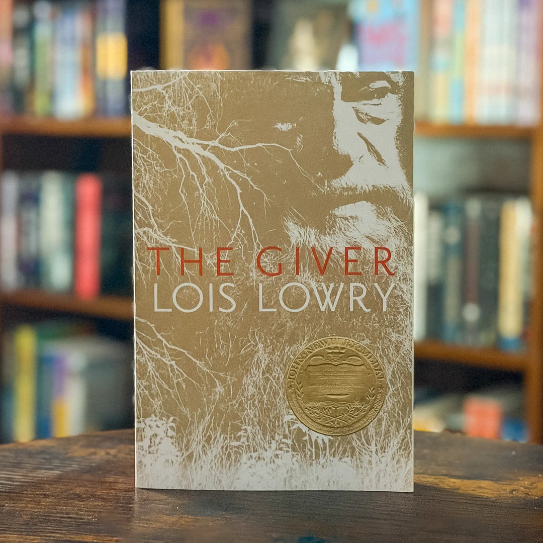 Book titled 'The Giver' by Lois Lowry with a gold and white cover on a wooden surface.