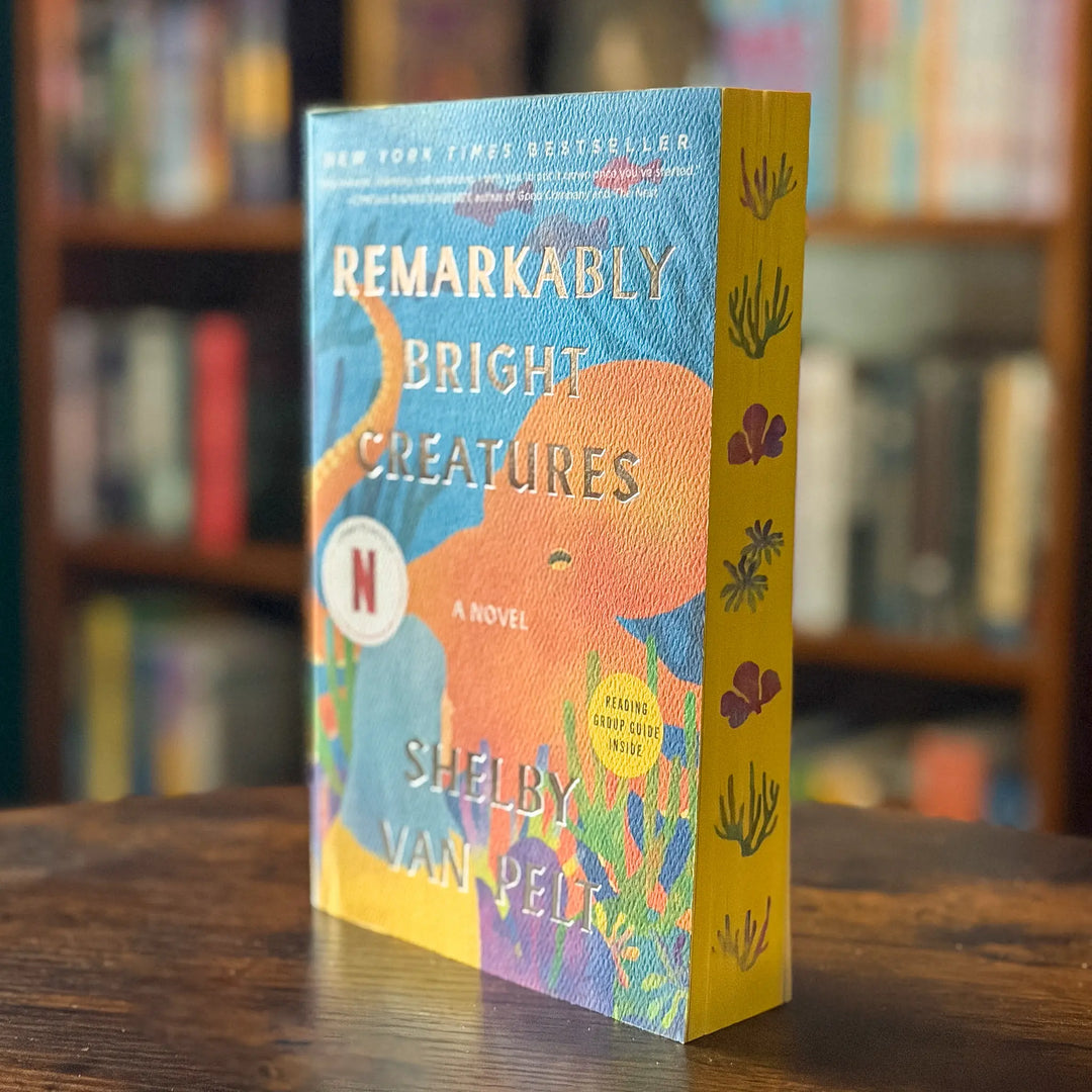 Book titled 'Remarkably Bright Creatures' by Shelby Van Pelt on a wooden surface with a blurred bookshelf background.