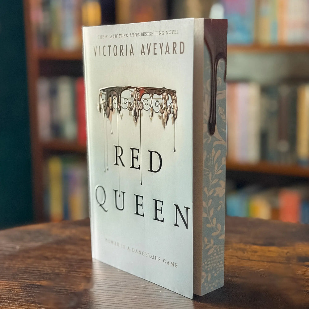 Book titled 'Red Queen' by Victoria Aveyard on a wooden surface with a blurred bookshelf background.