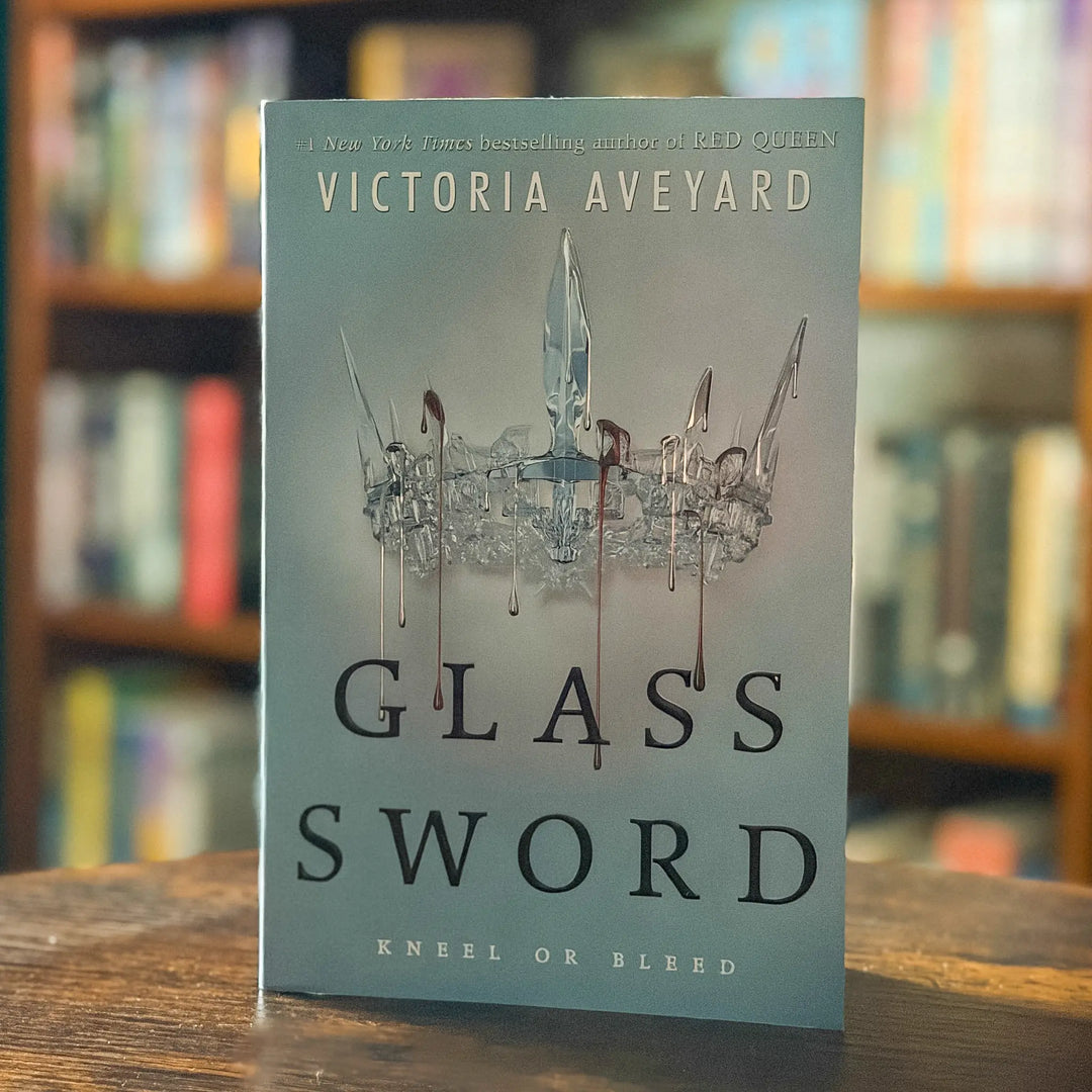 Book titled 'Glass Sword' by Victoria Aveyard on a wooden surface with a blurred bookshelf background.