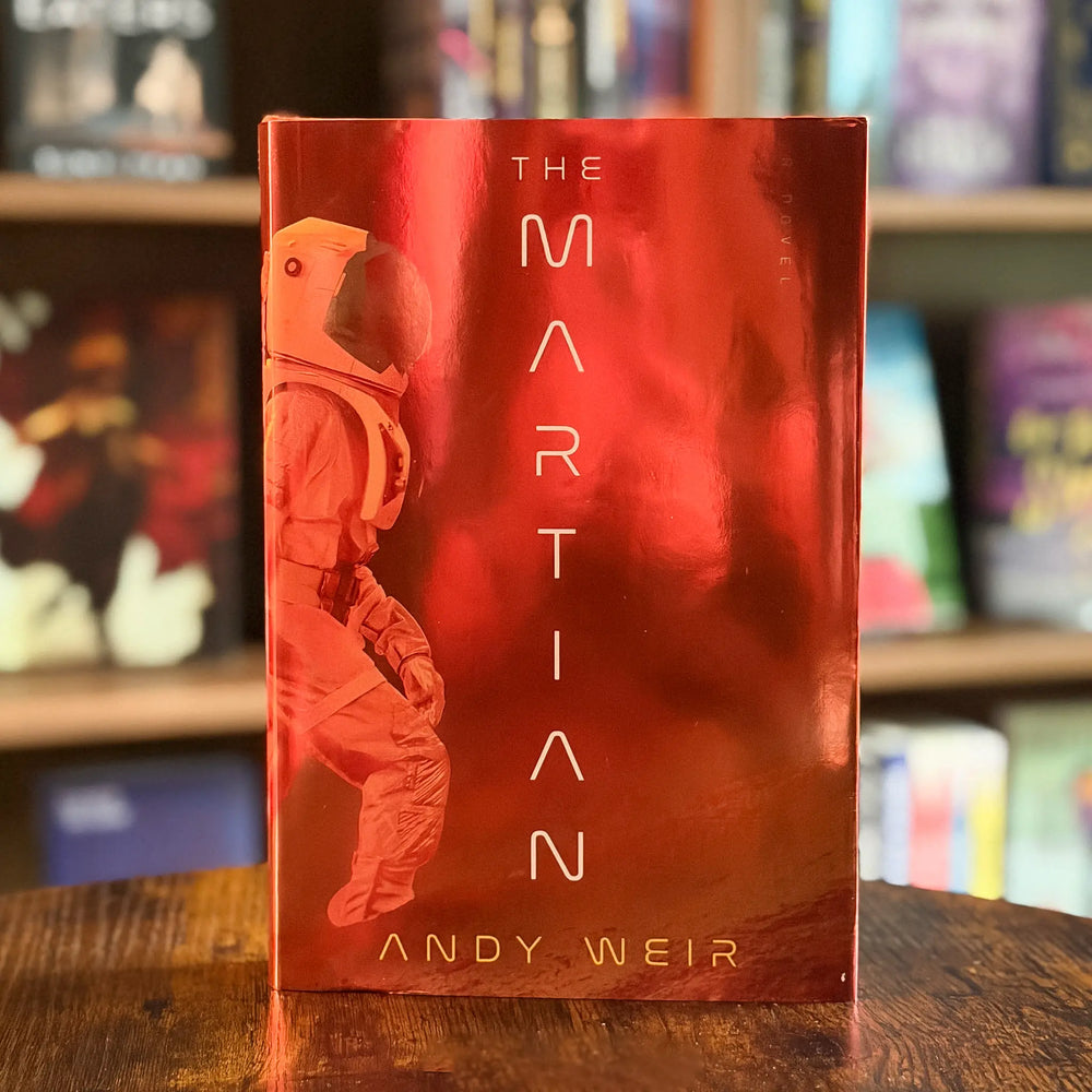 Book titled 'The Martian' by Andy Weir with a red cover featuring an astronaut silhouette on a wooden surface.
