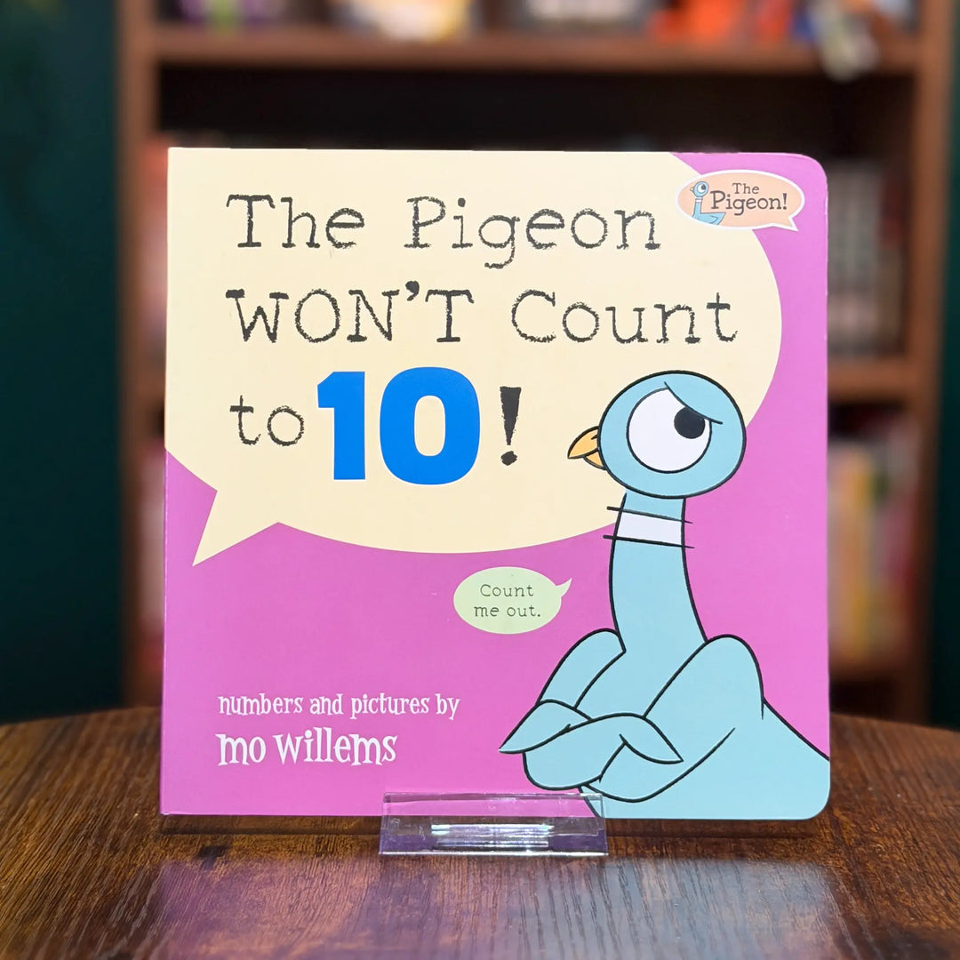 Children's book titled 'The Pigeon WON'T Count to 10!' by Mo Willems on a wooden surface with a blurred bookshelf background.
