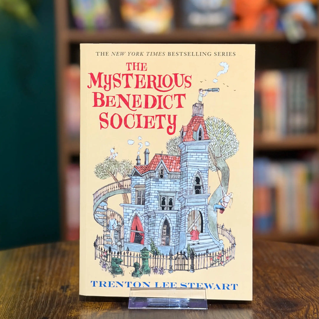Book titled 'The Mysterious Benedict Society' by Trenton Lee Stewart on a wooden surface with a blurred bookshelf background.