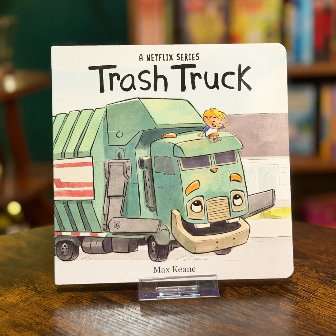 Children's book titled 'Trash Truck' by Max Keane on a wooden surface with a blurred bookshelf background.