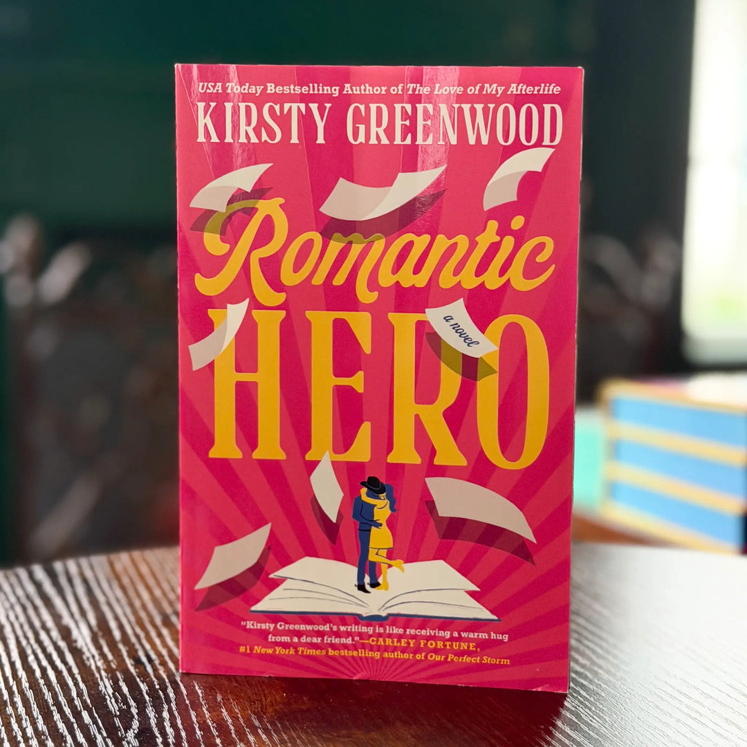 Book titled 'Romantic Hero' by Kirsty Greenwood on a wooden surface with a blurred background.