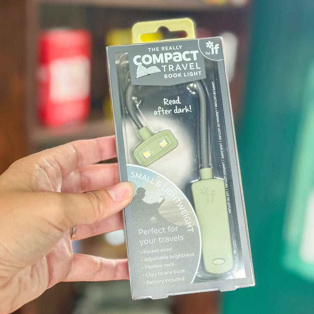Hand holding a package of a compact travel book light with branding and product details.