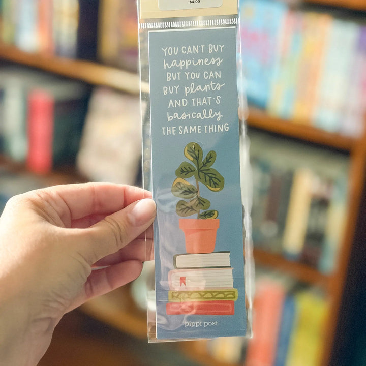 Hand holding a bookmark with a plant and book illustration and text in front of a bookshelf.