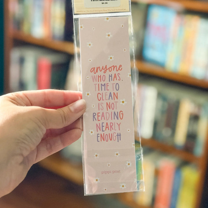 Hand holding a colorful bookmark with text in front of a bookshelf.
