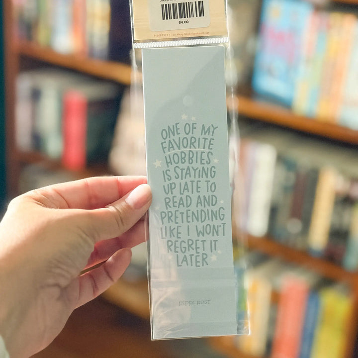 Hand holding a bookmark with a humorous quote in front of a bookshelf.