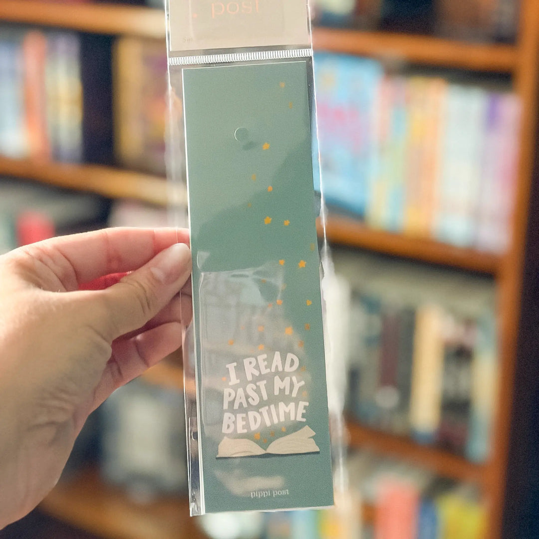 Hand holding a green bookmark with text in front of a bookshelf.
