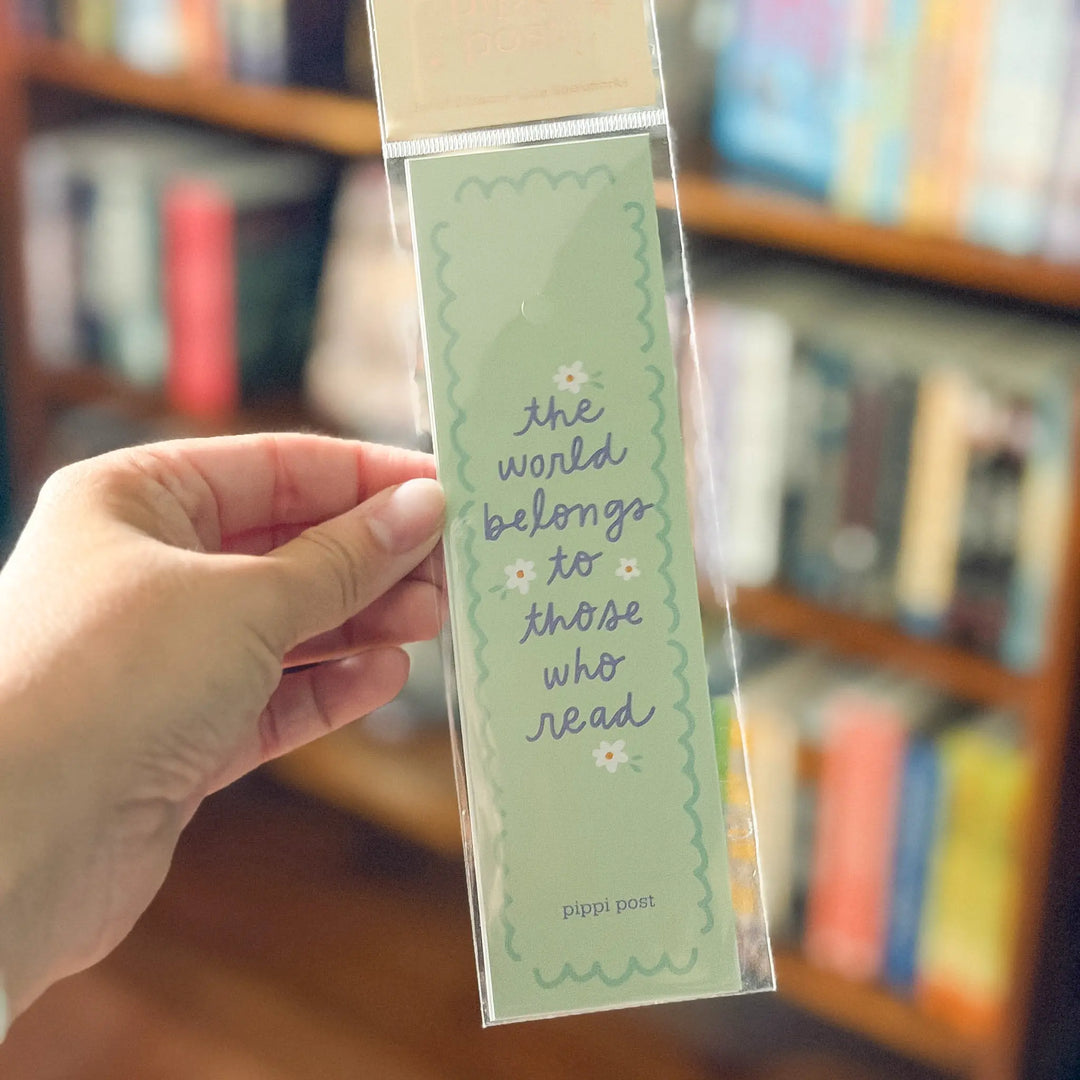 Hand holding a green bookmark with text in front of a bookshelf
