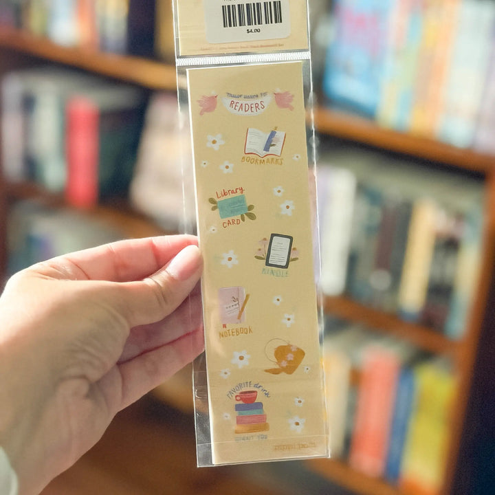 Packaged bookmark with illustrations held in front of a bookshelf