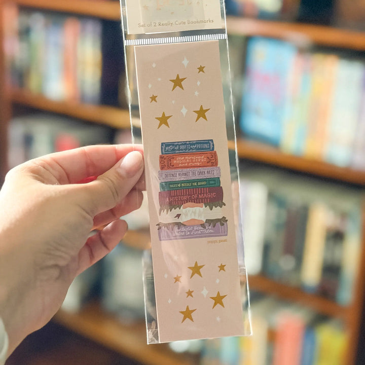 Hand holding a decorative bookmark with stars and text in front of a bookshelf.