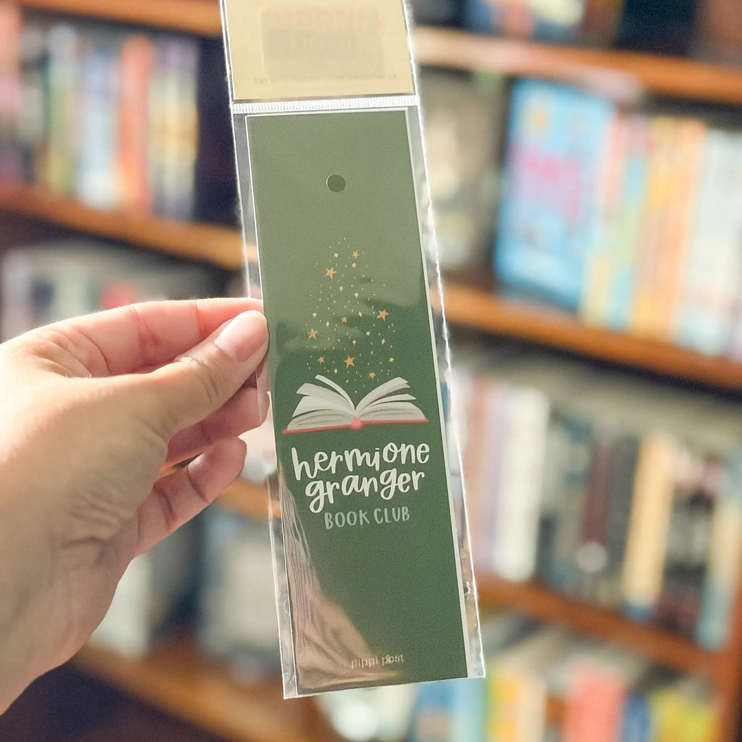 Hand holding a green bookmark with text against a blurred bookshelf background.