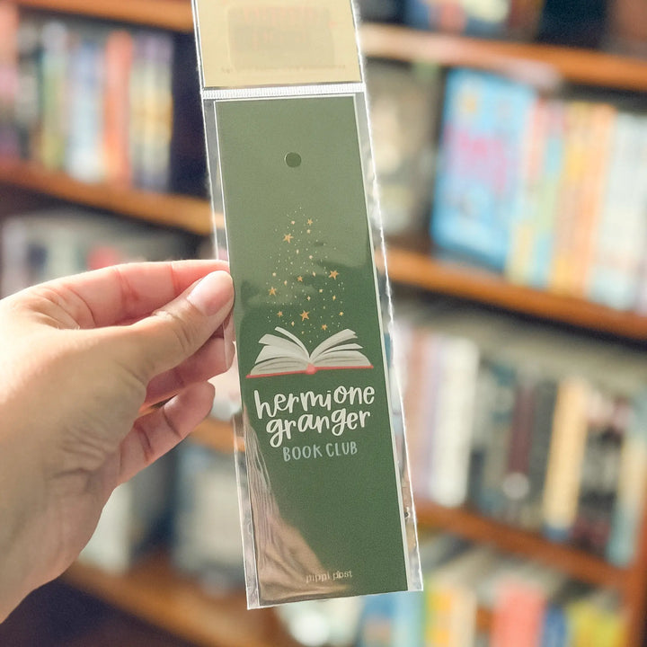 Hand holding a green bookmark with text against a blurred bookshelf background.