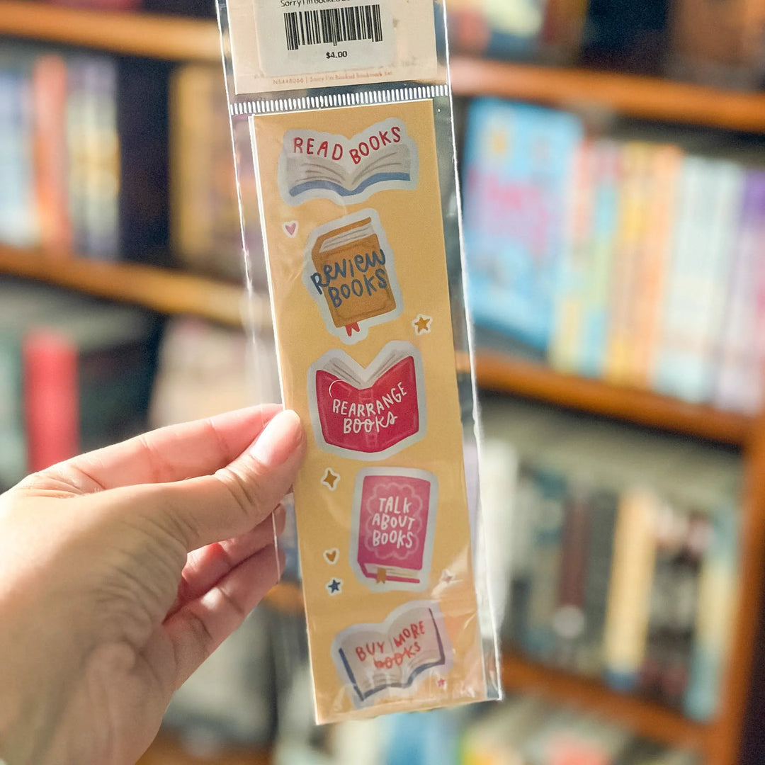 Packaged bookmark with colorful designs held in front of a bookshelf.