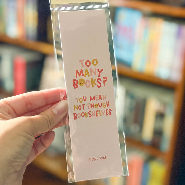 Hand holding a colorful bookmark with text in front of a bookshelf.