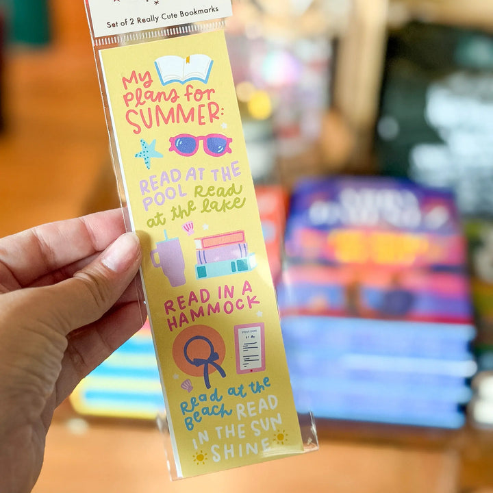 Hand holding a colorful bookmark with summer reading activities on a blurred background