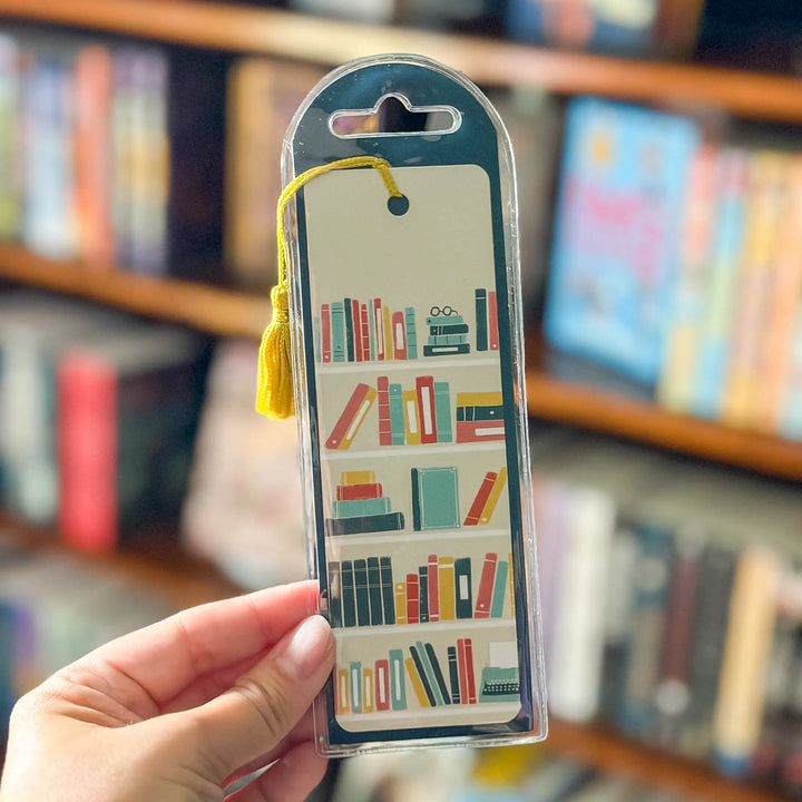 Packaged bookmark with book design held in front of a bookshelf