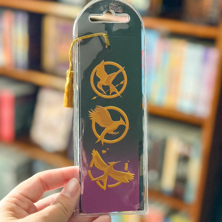 Bookmarks with bird symbols in packaging held by a hand against a blurred bookshelf background