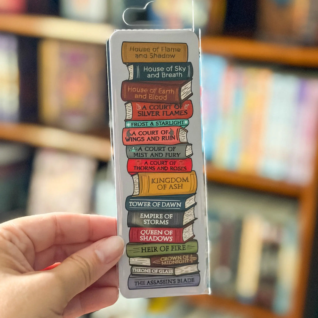 Colorful book title bookmark in packaging held by a hand with blurred bookshelf background