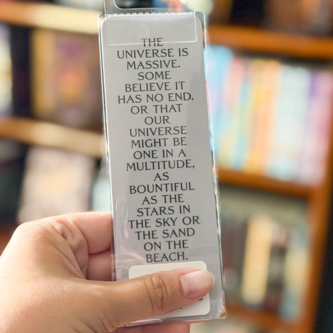 Hand holding a bookmark with text about the universe in front of a blurred bookshelf.