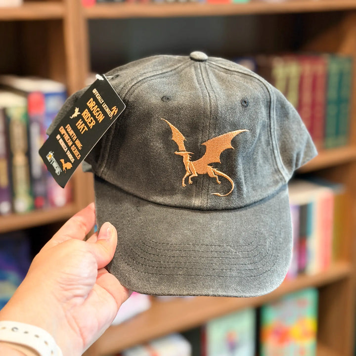 Gray cap with dragon emblem held in front of a bookshelf