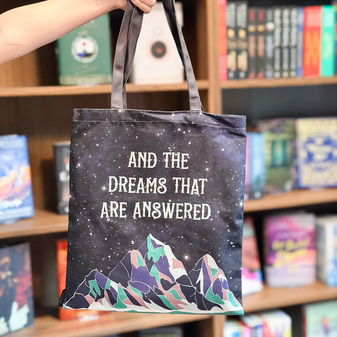 Tote bag with mountain design and text held in front of a bookshelf