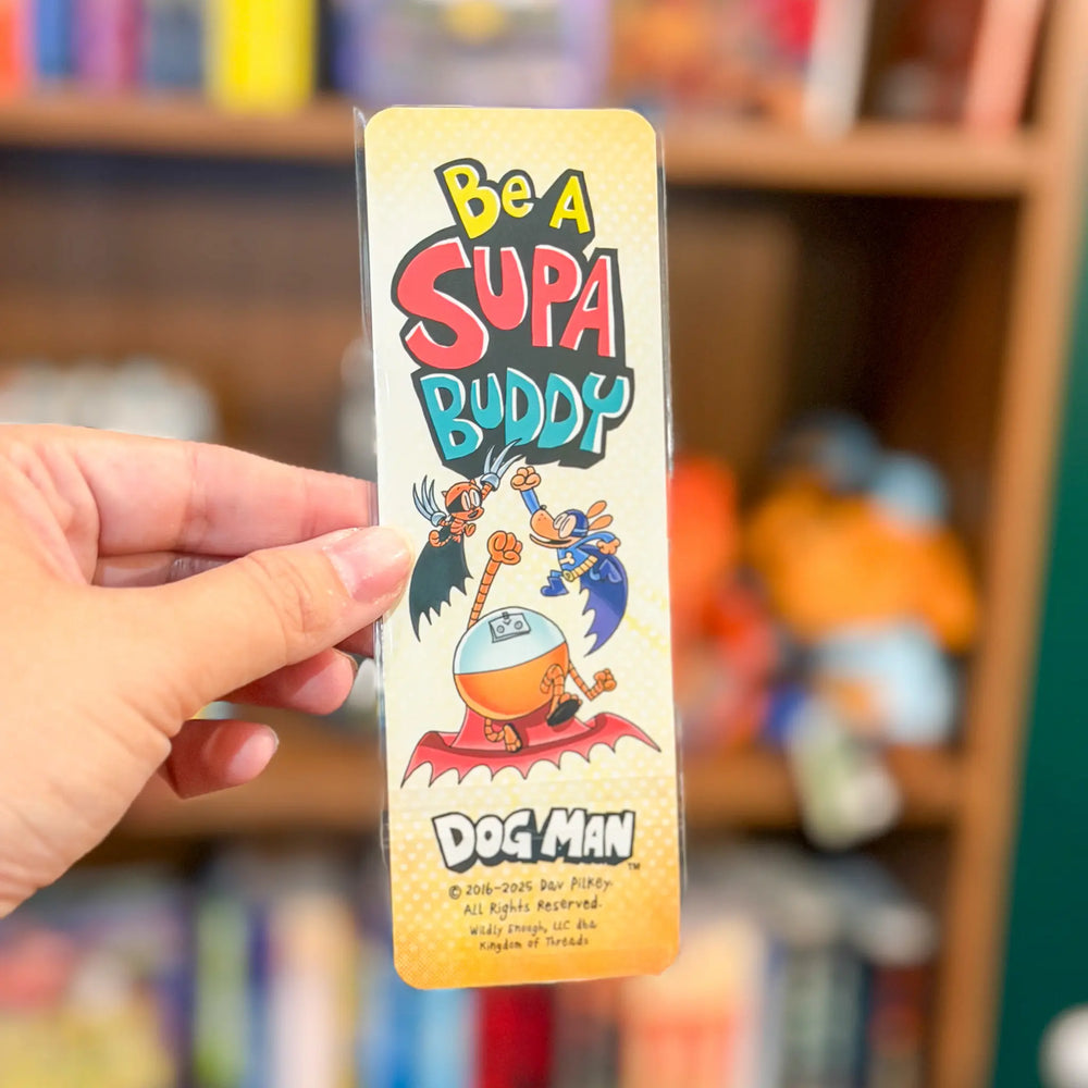 Hand holding a 'Be a Supa Buddy' bookmark with cartoon character design in front of a bookshelf.