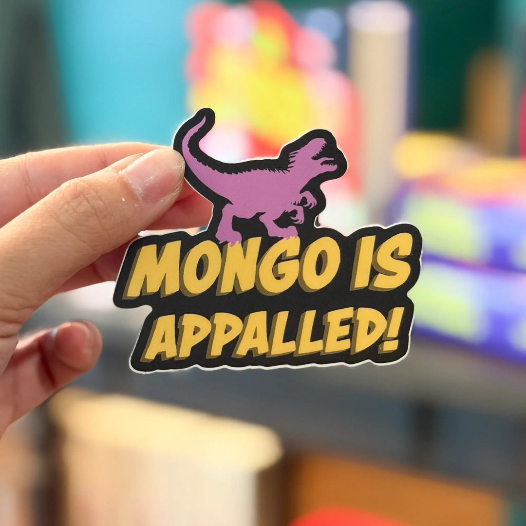 Hand holding a sticker with a dinosaur and text 'MONGO IS APPALLED!' against a colorful blurred background.