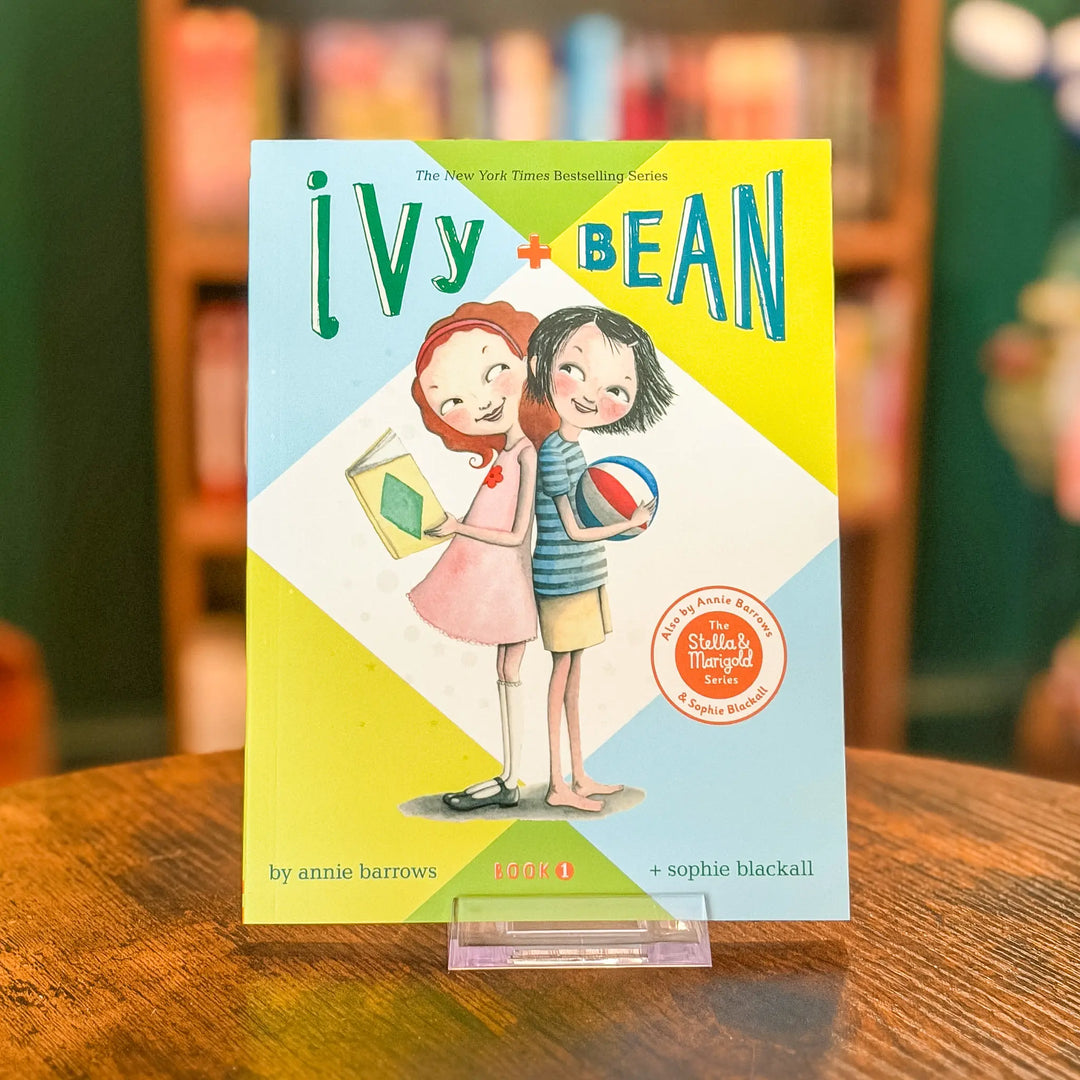 Book titled 'Ivy + Bean' on a wooden surface with a blurred bookshelf background