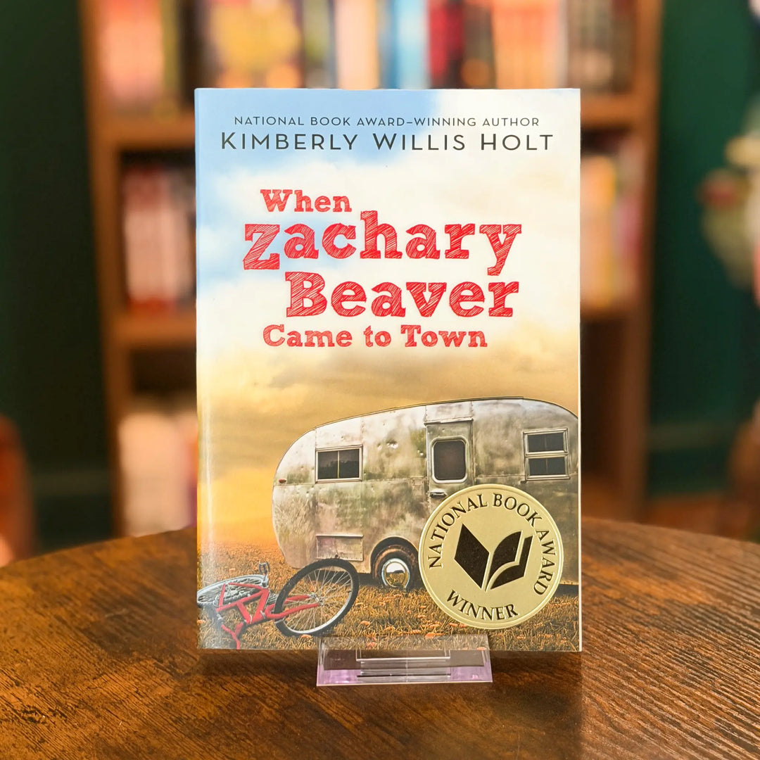 Book titled 'When Zachary Beaver Came to Town' by Kimberly Willis Holt on a wooden surface with a blurred bookshelf background.