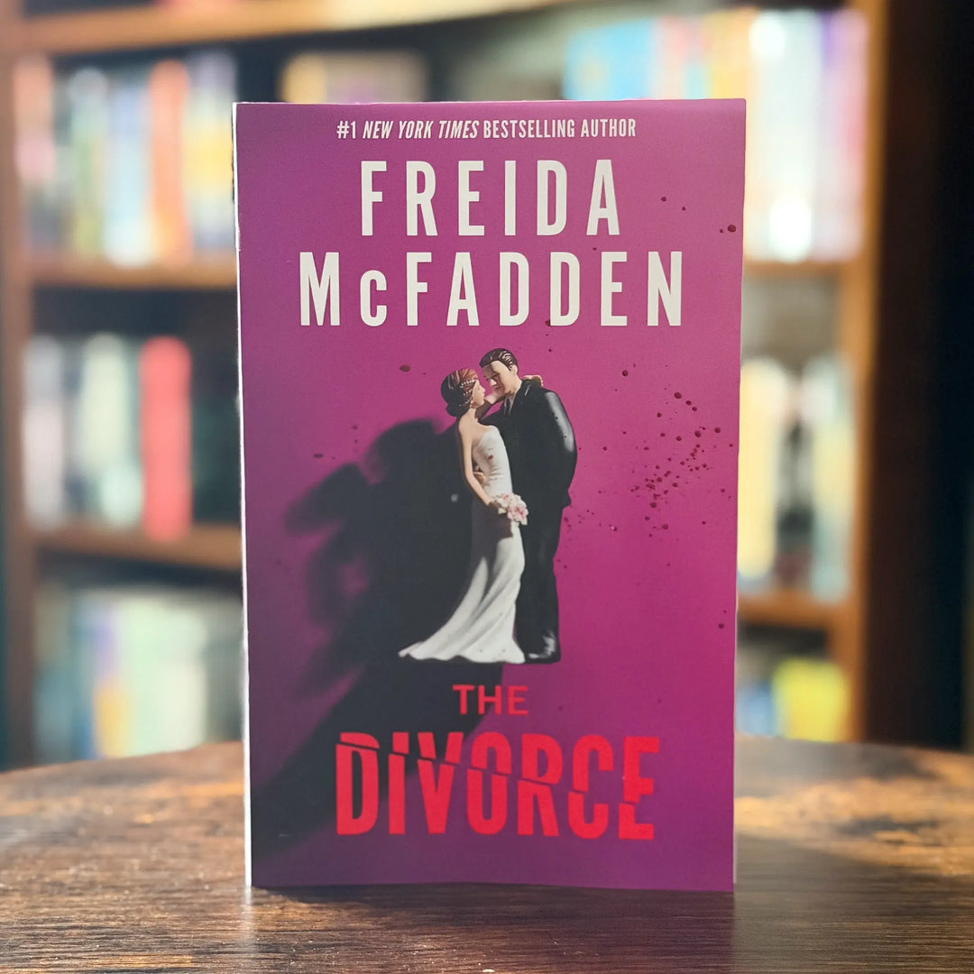 Book titled 'The Divorce' by Freida McFadden on a wooden surface with blurred bookshelf background