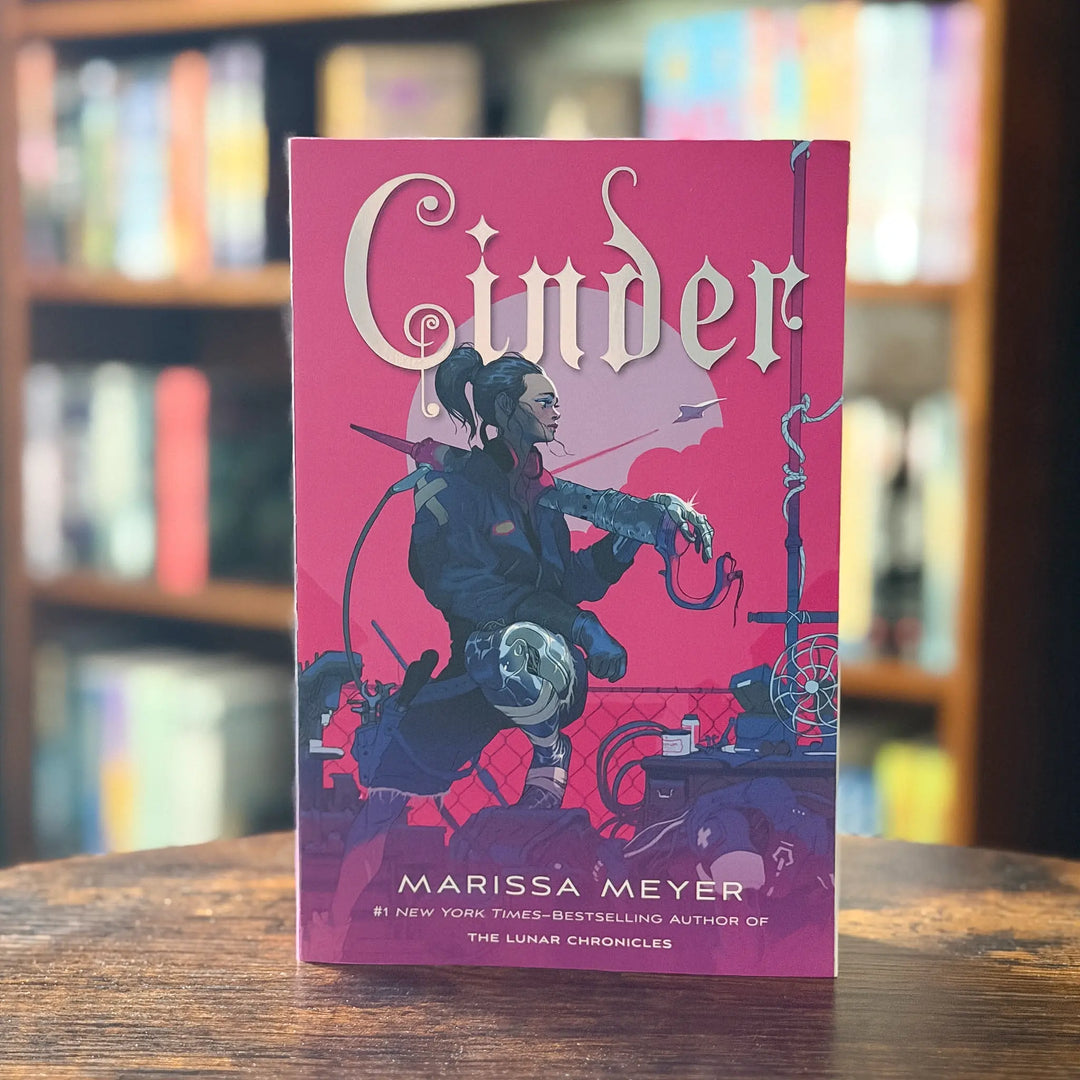 Book titled 'Cinder' by Marissa Meyer on a wooden surface with a blurred bookshelf background