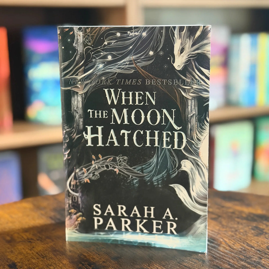 Book titled 'When the Moon Hatched' by Sarah A. Parker on a wooden surface with a blurred bookshelf background.