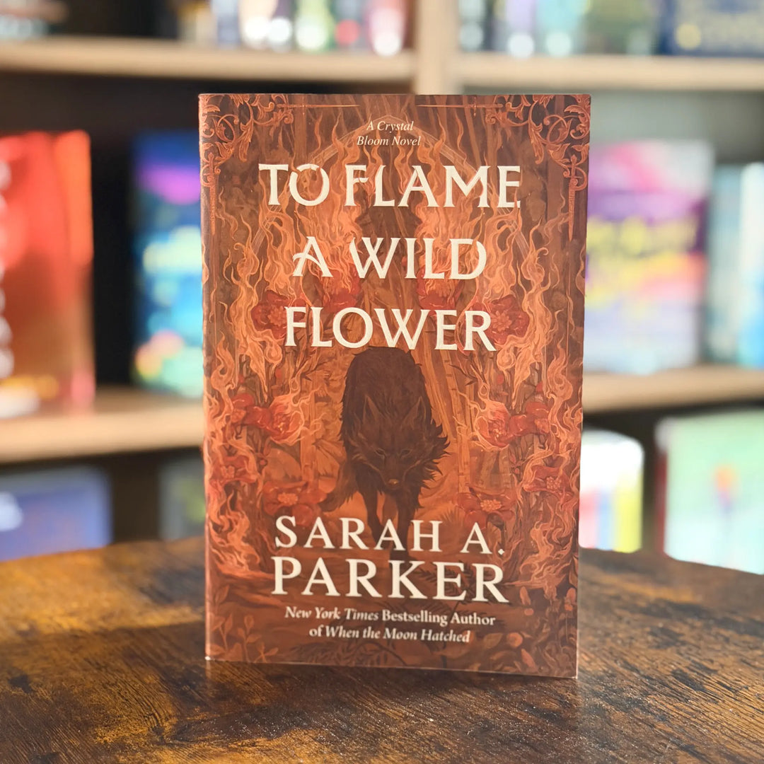 Book titled 'To Flame a Wild Flower' by Sarah A. Parker on a wooden surface with a blurred bookshelf background.