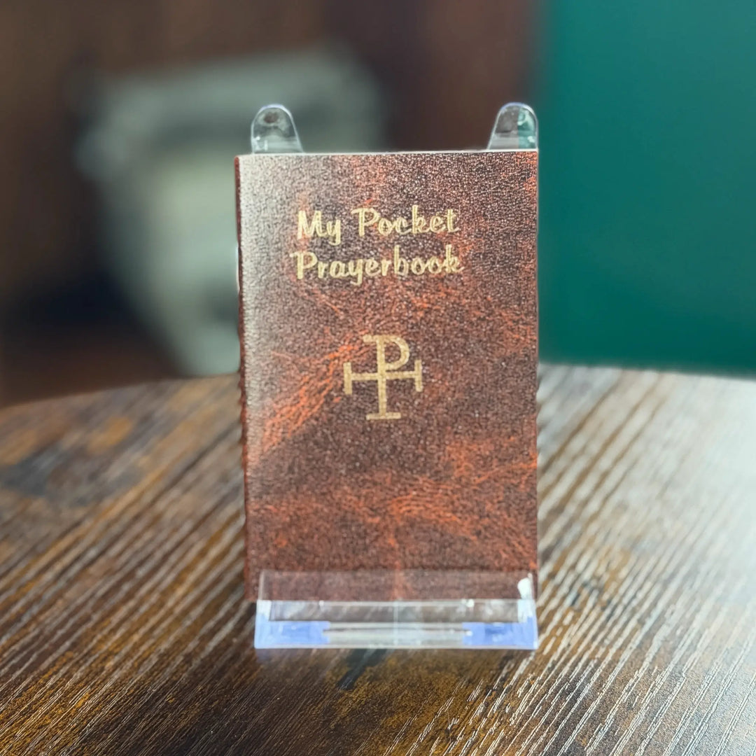 Small leather-bound book titled 'My Pocket Prayerbook' on a stand with a blurred background
