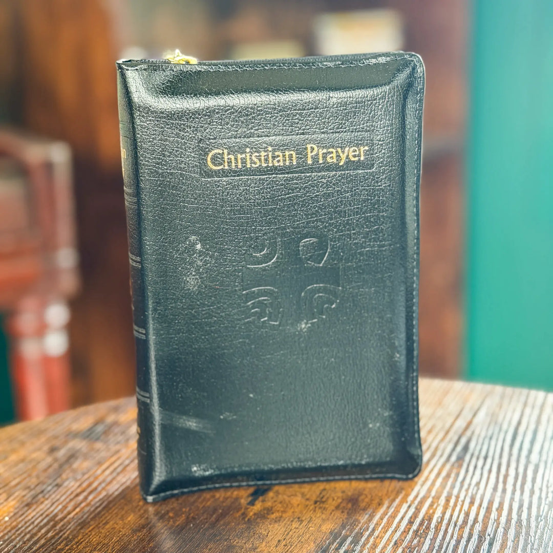 Black leather prayer book titled 'Christian Prayer' on a wooden surface.
