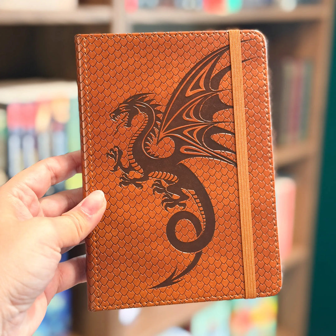 Brown notebook with dragon design held by a hand in a library setting