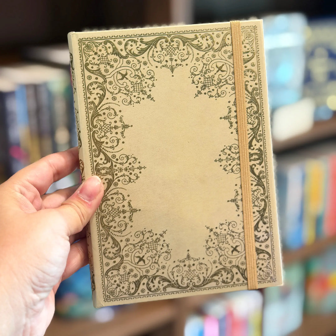Hand holding a decorative notebook with a blurred bookshelf background