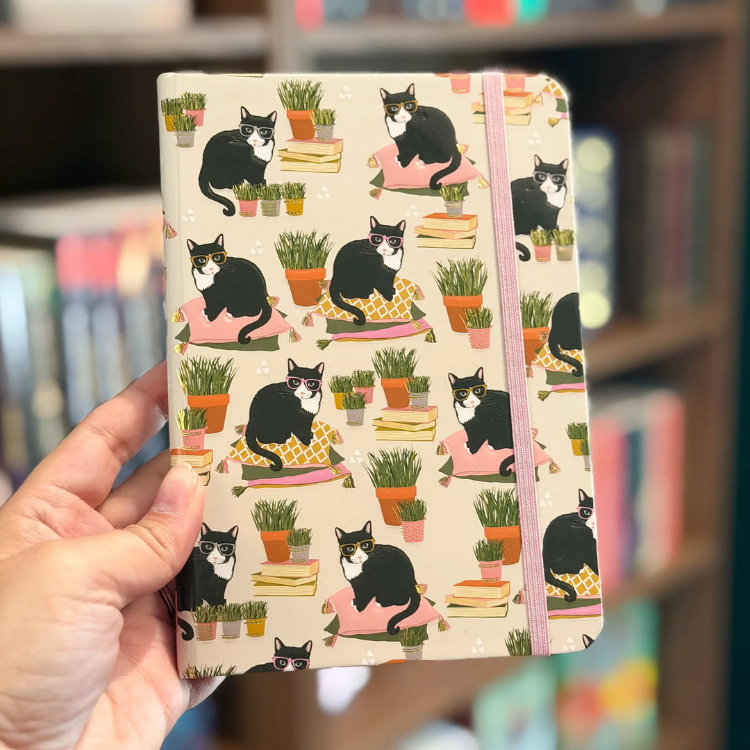 Notebook with cat and plant pattern held by a hand against a blurred background