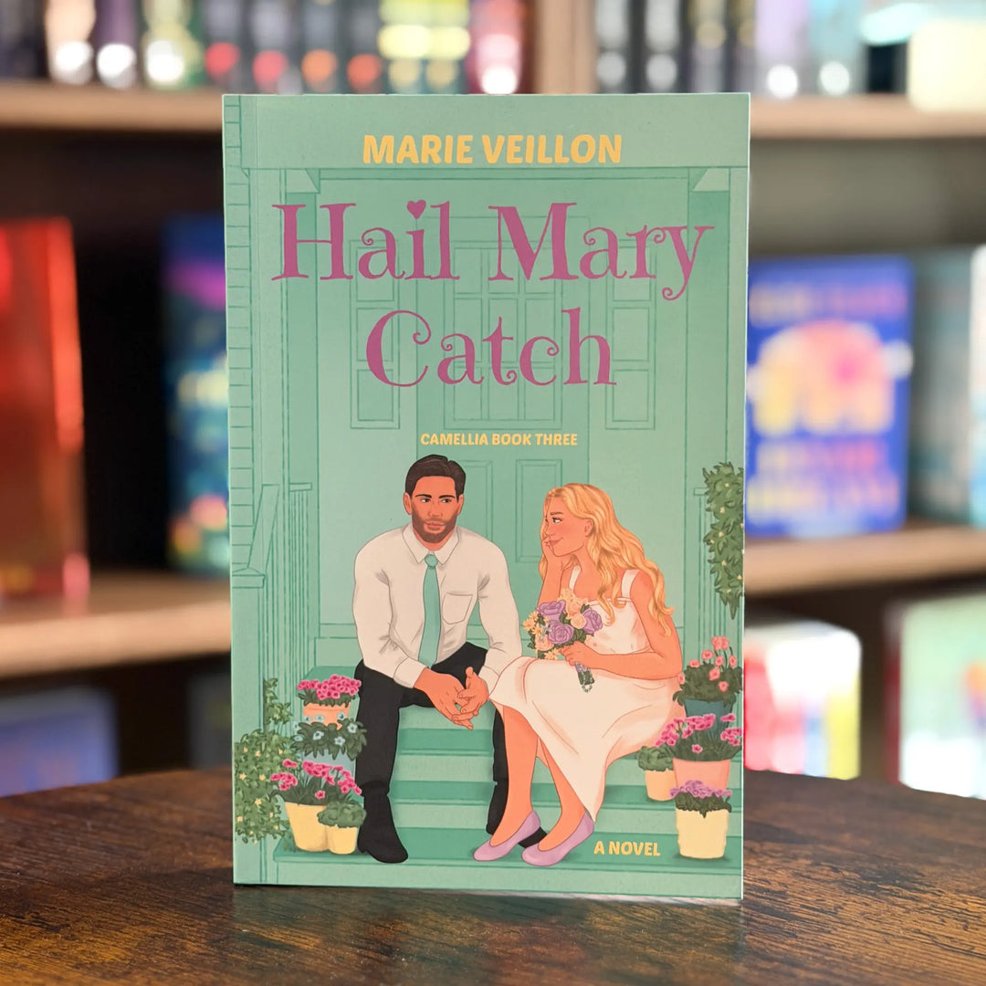 Book cover of 'Hail Mary Catch' by Marie Veillon on a wooden surface with blurred bookshelf in the background.