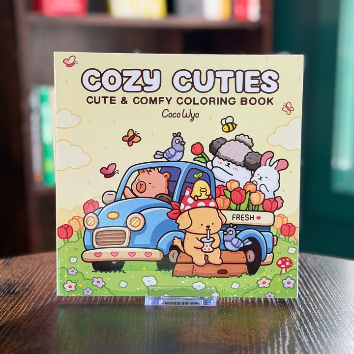 Cozy Cuties coloring book on a wooden surface with a blurred background