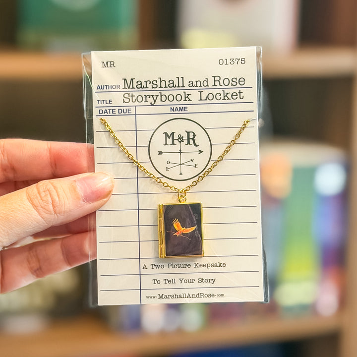 Gold necklace with a book-shaped pendant on a card labeled &