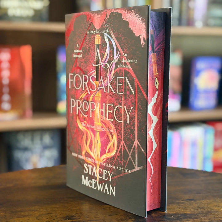 A hardcover book titled "A Forsaken Prophecy" by Stacey McEwan, standing upright on a wooden table with blurred bookshelves in the background.