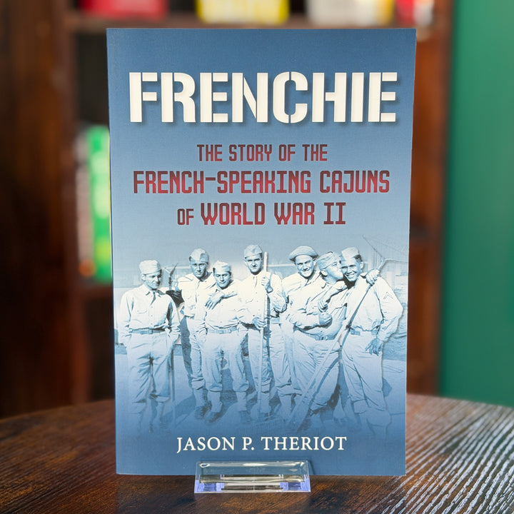 A book titled "FRENCHIE: The Story of the French-Speaking Cajuns of World War II" by Jason P. Theriot, standing upright on a clear acrylic display stand on a wooden table.