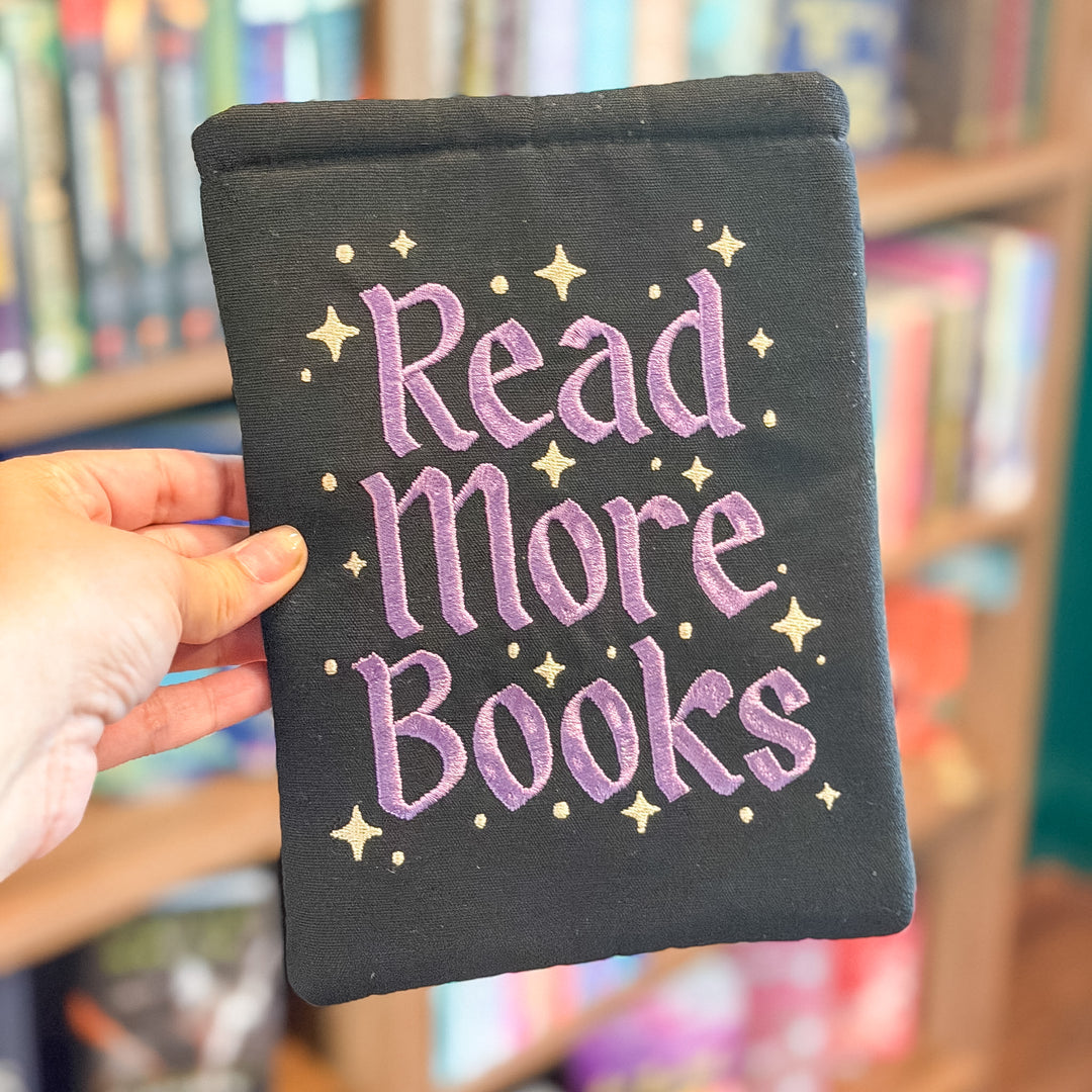 A hand holds a black fabric book pouch with purple embroidered text reading &