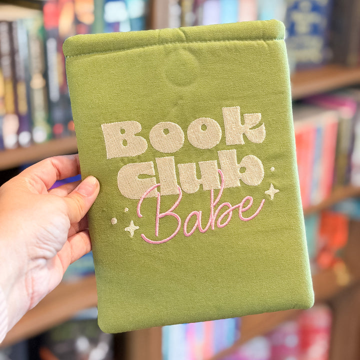 A hand holding a sage green fabric book club sign or pouch with &