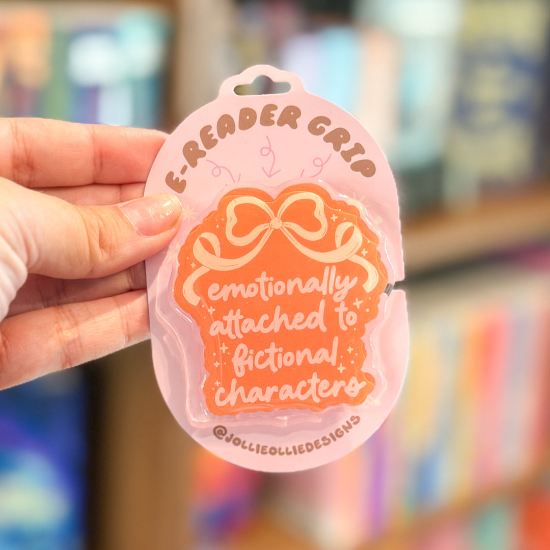 A hand holds a pink and orange sticker shaped like a book cover with the text &